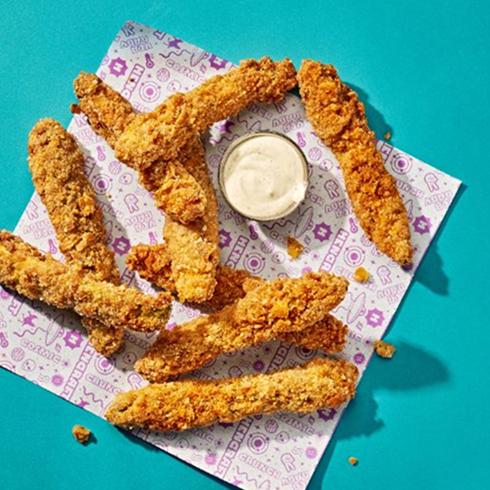 Nine Hencraft Great Big Tenders on patterned paper with a cup of dipping sauce.