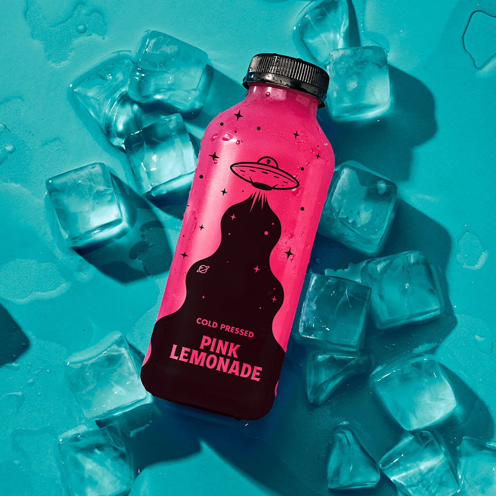 A bottle of Hencraft pink lemonade sits on a blue surface surrounded by ice cubes.
