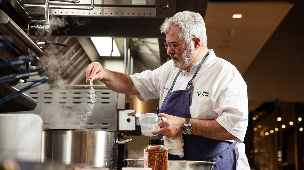 A Hencraft chef sprinkles salt into a steaming pot in a professional kitchen.